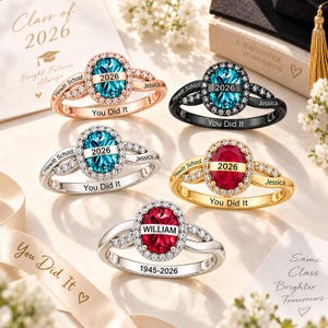 Könnte beinhalten: Fünf Ringe mit ovalem Schliff, zentralen blauen oder roten Steinen und kleinen klaren Steinen. Jeder Ring ist mit Hewitt School, Jessica, 2026 oder William sowie dem Schriftzug You Did It graviert. Die Ringe sind in Roségold, Schwarz, Silber und Gold.