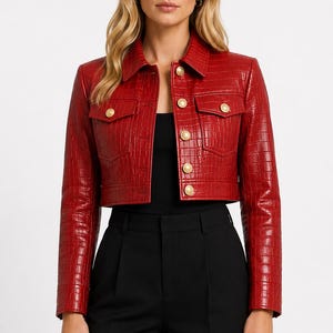 Könnte beinhalten: Kurze rote Jacke mit Krokodilmuster. Die Jacke hat einen Kragen, zwei Brusttaschen und goldfarbene Knöpfe. Das Model trägt eine schwarze Hose und ein schwarzes Oberteil. Die Jacke ist etwa 40 cm lang.