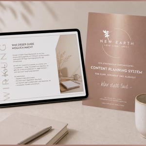Könnte beinhalten: Ein digitales Tablet zeigt Text auf Deutsch, neben einer Broschüre mit den Worten "New Earth" und "Content Planning System". Ein Notizbuch, ein Stift und eine Tasse sind ebenfalls vorhanden. Das Farbschema ist hauptsächlich Roségold und Weiß.