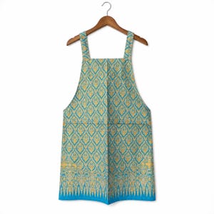 May include: A teal and gold apron with a decorative pattern, hanging on a wooden hanger. The apron has a square neckline, shoulder straps, and a large front pocket. The bottom edge features a detailed border.