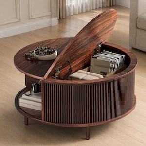 May include: A round, dark wood coffee table with a lift-up lid revealing storage. The table has a fluted side and sits on short legs. A bowl of cherries and a camera are visible on the table's surface. The open lid reveals books and other items.