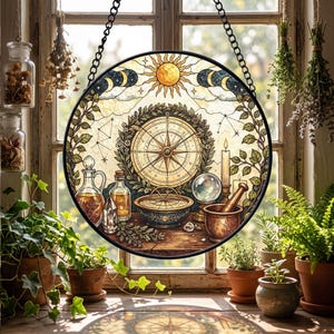 May include: A circular stained glass suncatcher featuring a central compass surrounded by a wreath, a sun, moon phases, and constellations. Below are glass bottles, a crystal, a bowl, a crystal ball, a candle, and a mortar and pestle.
