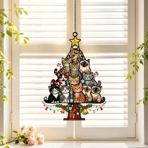 May include: A stained glass suncatcher shaped like a Christmas tree, featuring a stack of various cat breeds in different colors. The tree is topped with a yellow star, decorated with candy canes, bells, and a gift box at the base, hanging by a chain.