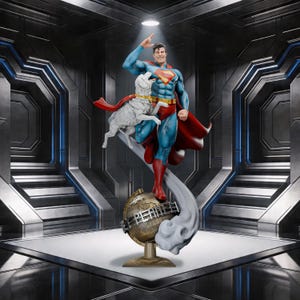 Puede incluir: Una estatua de Superman en una pose dinámica, saludando con una sonrisa. La figura lleva un traje azul y rojo, con una capa roja. Un perro blanco con una capa roja está al lado de Superman. La estatua está sobre una base de globo con la palabra "Planet".