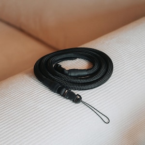 Pu&ograve; includere: Un cordino nero arrotolato, con una trama intrecciata, dotato di un fermaglio in plastica e un piccolo anello. Il cordino &egrave; progettato per essere indossato al collo o al polso, adatto per chiavi, un telefono o un badge.
