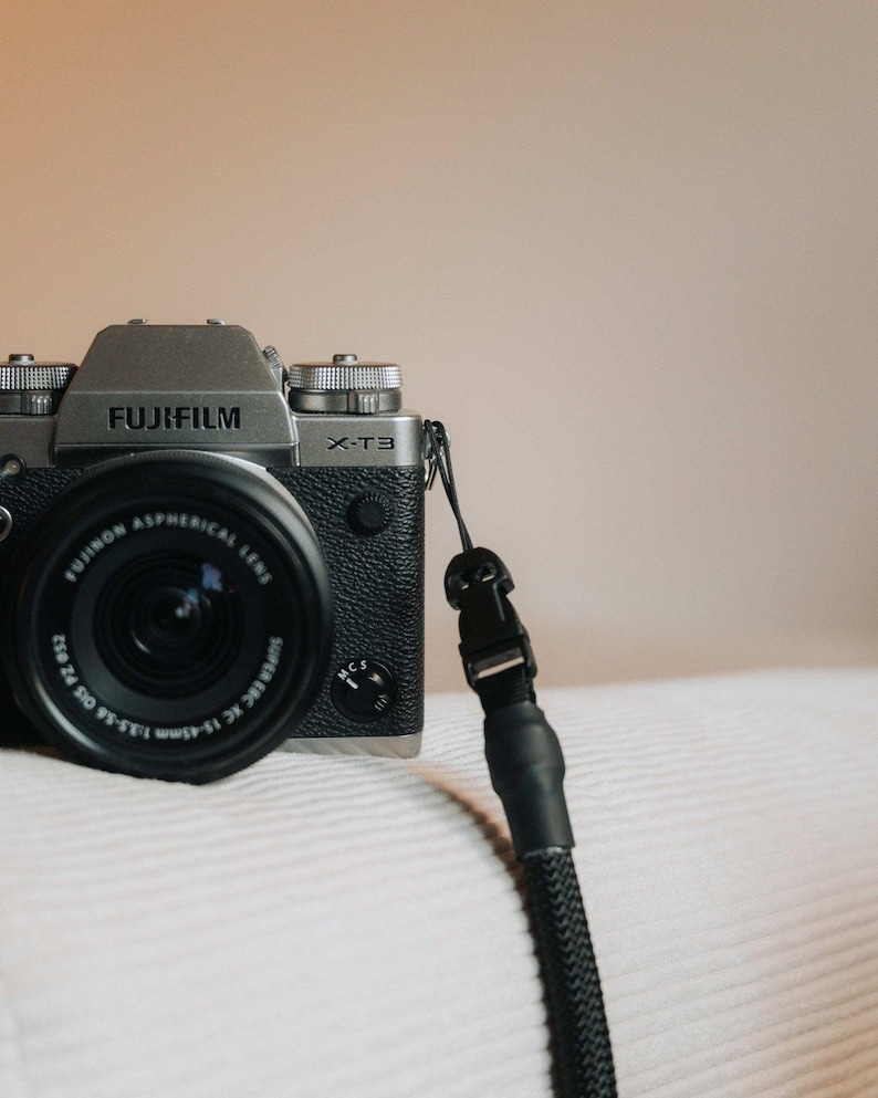 Pu&ograve; includere: Una fotocamera Fujifilm X-T3 argento e nera con obiettivo e cinturino neri. La fotocamera &egrave; su una superficie bianca. L'obiettivo ha la scritta "FUJINON ASPHERICAL LENS" e il corpo macchina "FUJIFILM X-T3".
