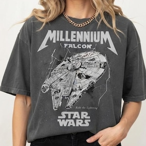Może przedstawiać: Ciemnoszary t-shirt z krótkim rękawem z białą grafiką statku kosmicznego Millennium Falcon. Projekt zawiera napis Millennium Falcon i Star Wars oraz frazę Ride the Lightning w postarzanym, inspirowanym stylem vintage wyglądzie.