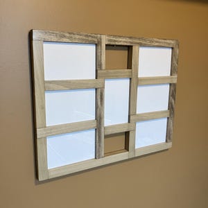 May include: A multi-opening photo frame with a geometric design. The frame is constructed from light-colored wood with a weathered finish. It features multiple rectangular openings with white backgrounds, creating a grid-like pattern.