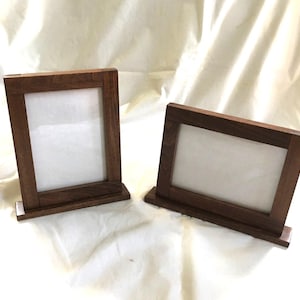 May include: Two wooden picture frames with a dark brown finish. Each frame has a rectangular opening with a white backing. The frames are designed to stand upright on a flat surface.