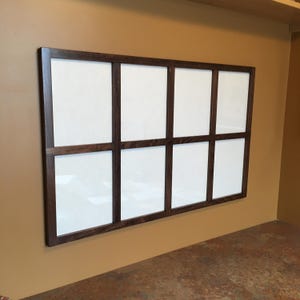 May include: A dark brown wood picture frame with nine rectangular openings. The frame is mounted on a tan wall.