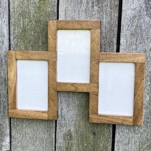 May include: A wooden multi-photo frame with three rectangular openings. The frame is constructed from light brown wood and is mounted on a weathered wooden surface. The openings are filled with white backing.