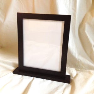 May include: A black picture frame with a stand. The frame is made of wood and has a simple design.