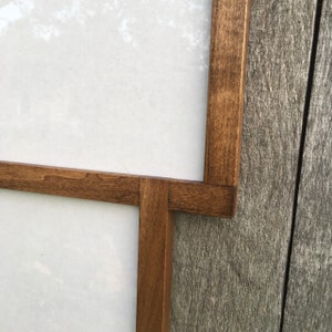 May include: Close-up of a wooden frame with a white background. The frame is made of dark brown wood and has a simple design.