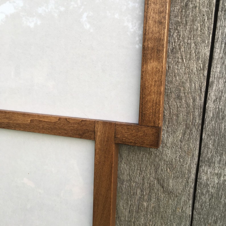 May include: Close-up of a wooden frame with a white background. The frame is made of dark brown wood and has a simple design.