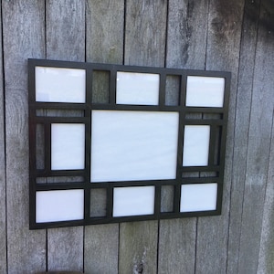 May include: A black picture frame with multiple openings for photos. The frame has a modern design with a rectangular shape and a black finish.