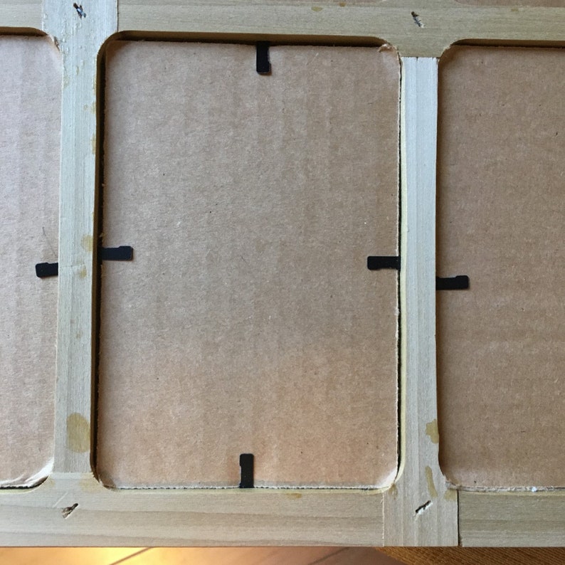 May include: A wooden picture frame with three openings, each with a cardboard backing and black paper tabs for holding the picture in place.