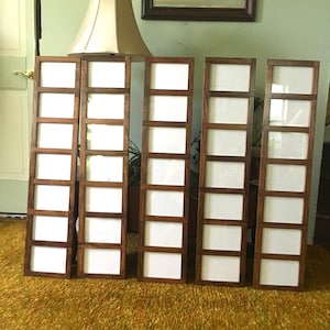 May include: Four brown wooden picture frames with white mats. Each frame has eight openings for photos. The frames are arranged in a row on a brown carpet.