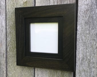 May include: A black wood picture frame with a white mat and a clear glass front. The frame is hanging on a wooden wall.