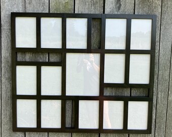 May include: A large rectangular dark brown wooden collage picture frame featuring multiple openings of varying sizes arranged in a grid pattern. The frame has a smooth finish and holds several white rectangular inserts within its structure.