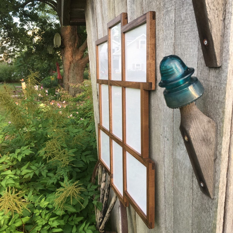 May include: A wooden picture frame with nine individual frames, each with a white background. The frame is mounted on a wooden wall with a blue glass insulator.
