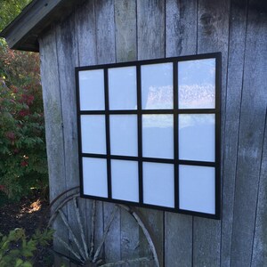 May include: A black picture frame with 12 individual square openings. The frame is mounted on a wooden wall.