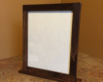 May include: A dark brown wooden picture frame with a stand. The frame is empty and ready for a photo.