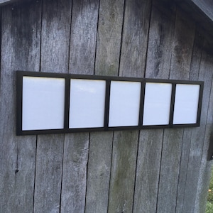 May include: A black picture frame with five openings, each with a white mat. The frame is mounted on a wooden wall.