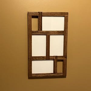 May include: A rectangular wooden wall-mounted photo frame with a dark brown finish. The frame has a geometric design with five white spaces for photos. The frame is mounted on a tan wall.