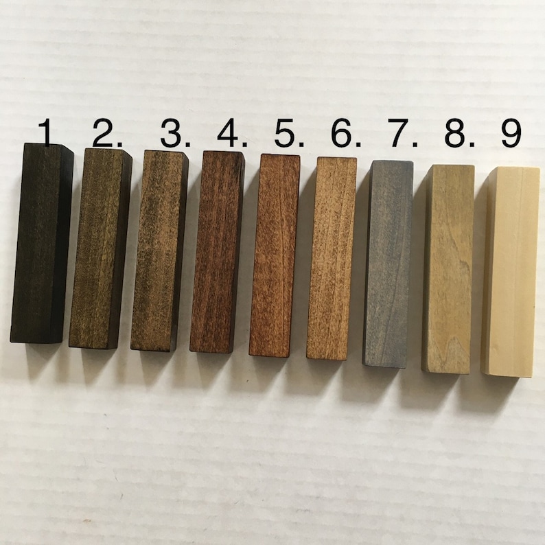 May include: Nine wood samples stained in different colors, numbered 1 through 9. The colors range from dark brown to light brown, gray, and natural wood.