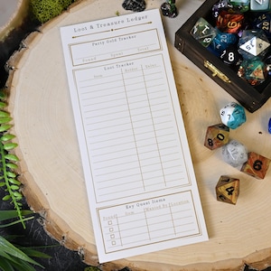 May include: A Loot & Treasure Ledger notepad with a Party Gold Tracker and Key Quest Items sections. The notepad is on a wooden surface, surrounded by various polyhedral dice and a wooden box filled with more dice.