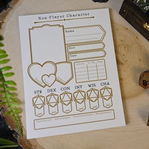 May include: A white Non-Player Character sheet with gold-colored text and design elements. The sheet includes sections for name, race, class, and stats, along with a heart and shield graphic. Dice are scattered around the sheet, suggesting a tabletop game.