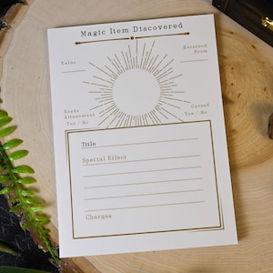 May include: A white card with gold text and a sunburst design, labeled "Magic Item Discovered." It includes sections for "Value," "Title," and "Special Effect." Dice and a wooden box are in the background.