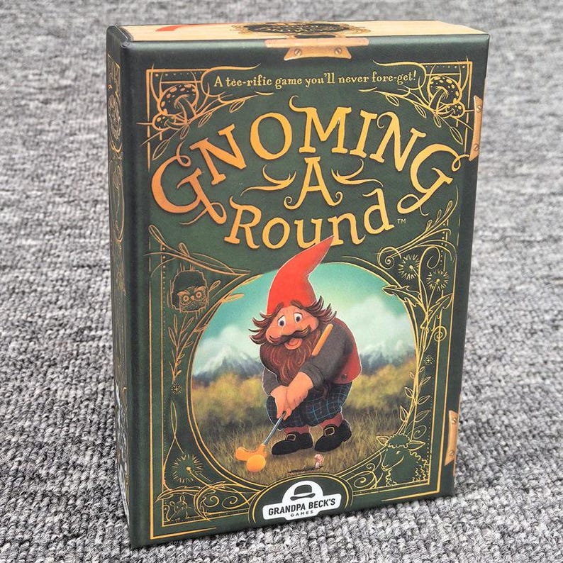 K&ouml;nnte beinhalten: Eine rechteckige Kartenspielschachtel mit dem Titel Gnoming A Round, dunkelgr&uuml;nem Hintergrund und goldenen Zierr&auml;ndern. Die Vorderseite zeigt eine Illustration eines Gnoms beim Golfspielen sowie den Text A tee-rific game you'll never fore-get! und Grandpa Beck's Games.