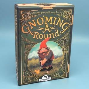 K&ouml;nnte beinhalten: Eine rechteckige Brettspielschachtel mit dem Titel Gnoming A Round auf dunkelgr&uuml;nem Hintergrund mit goldenen Akzenten. Das Cover zeigt eine Illustration eines Gnoms, der Golf spielt, vor einer Bergkulisse und dem Text A tee-rific game you'll never fore-get.