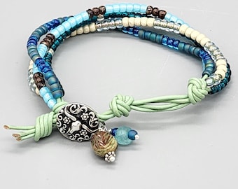 Pulsera de cuero con cuentas estilo bohemio: verde azulado, azul, cristal y botón plateado.