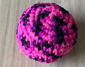 Pelota de ganchillo para hacky sack en combinación de rosa fucsia, morado y negro.
