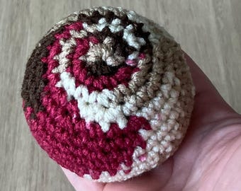 Pelota de ganchillo para hacky sack en combinación de marrón, granate, tostado y beige.
