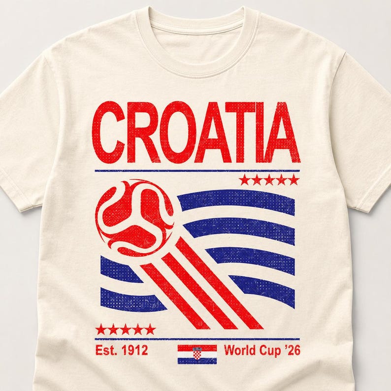 Pode incluir: Uma t-shirt de cor creme com um gr&aacute;fico desgastado que apresenta a palavra CROATIA em vermelho, uma bola de futebol estilizada, linhas onduladas azuis, riscas vermelhas, duas filas de cinco estrelas vermelhas, o texto Est. 1912, uma bandeira croata e World Cup '26.