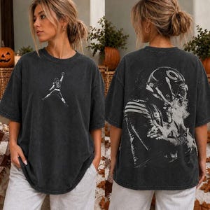 May include: A charcoal gray oversized t-shirt featuring a small white graphic of a football player in mid-air on the front chest and a large, detailed white graphic of a football player wearing a helmet on the back of the garment.