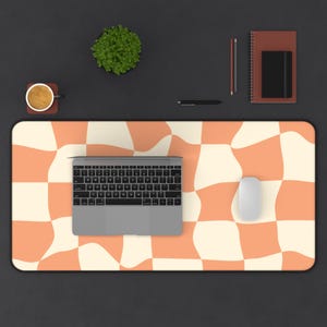 May include: A computer desk mat with a retro orange and cream checkerboard pattern. A laptop, mouse, and other office supplies are arranged on the mat. The mat is rectangular with rounded corners.