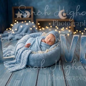 Op de afbeelding: Een pasgeboren baby gewikkeld in een blauwe deken en muts, genesteld in een zacht, lichtblauw bed. Het woord "LOVE" is geschreven in grote, blauwe houten letters. De achtergrond heeft een sterrennacht thema met feeërieke lichtjes.