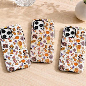 May include: Three rectangular smartphone cases featuring a repeating Halloween-themed pattern. The design includes illustrations of cartoon characters, orange pumpkins, haunted houses, spider webs, and candy corn in shades of orange, purple, and black.