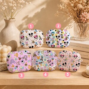 May include: Five rectangular protective cases for wireless earbuds, each featuring colorful patterns of classic cartoon characters. The designs include various character faces, sweets, and snacks on pastel backgrounds, labeled with numbers one through five.