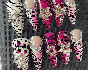 May include: A set of ten press-on nails featuring almond-shaped tips with various designs including black and white zebra stripes, pink and black leopard spots, and clear bases. Each nail is decorated with silver-toned star charms and rhinestones.