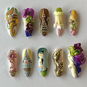 May include: Ten elaborately decorated artificial nails. The designs include floral patterns, gold detailing, and miniature sculptures. The colour scheme features pink, yellow, green, brown, and purple hues. Each nail is a miniature work of art.