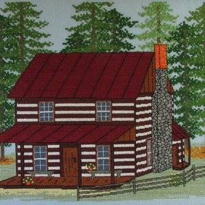 May include: A cross-stitch pattern of a brown log cabin with a red roof and a stone chimney. The cabin has a porch with a railing and two windows. There are green trees surrounding the cabin.