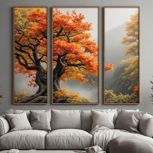 Könnte beinhalten: Ein dreiteiliges Wandbild-Set bestehend aus drei vertikalen gerahmten Paneelen. Das Kunstwerk zeigt einen knorrigen Baum mit leuchtend orangefarbenen und gelben Herbstblättern vor einem nebligen, grauen Bergpanorama als durchgehendes Motiv.