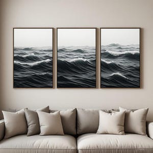 Peut inclure: Un ensemble de trois cadres muraux verticaux représentant un océan sombre et agité avec des vagues déferlantes et des crêtes d'écume blanche. L'œuvre présente une palette de couleurs monochromatiques dans des tons noir, gris et blanc.