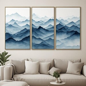 Peut inclure: Un ensemble de trois tableaux muraux verticaux encadrés représentant des chaînes de montagnes superposées dans des tons de bleu et de blanc. L'œuvre de style aquarelle montre des sommets qui se chevauchent avec des opacités variées.