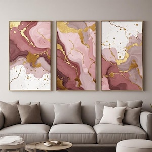 May include: A set of three rectangular wall art prints featuring an abstract fluid marble design in shades of dusty rose, deep burgundy, and white, accented with metallic gold veins and splatters, displayed in thin gold-toned frames.